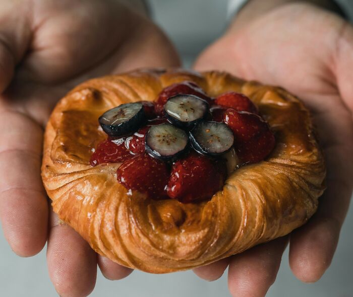 Hands holding a fresh pastry topped with strawberries and blueberries, highlighting European netizens’ common country facts.