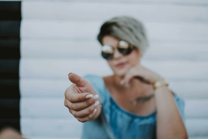 Blurred woman wearing sunglasses and blue top extending hand in a casual pose representing middle class lifestyle vibes