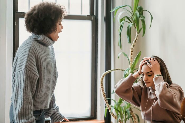 Two women showing dark truths of human behavior, one yelling while the other holds her head in distress indoors.