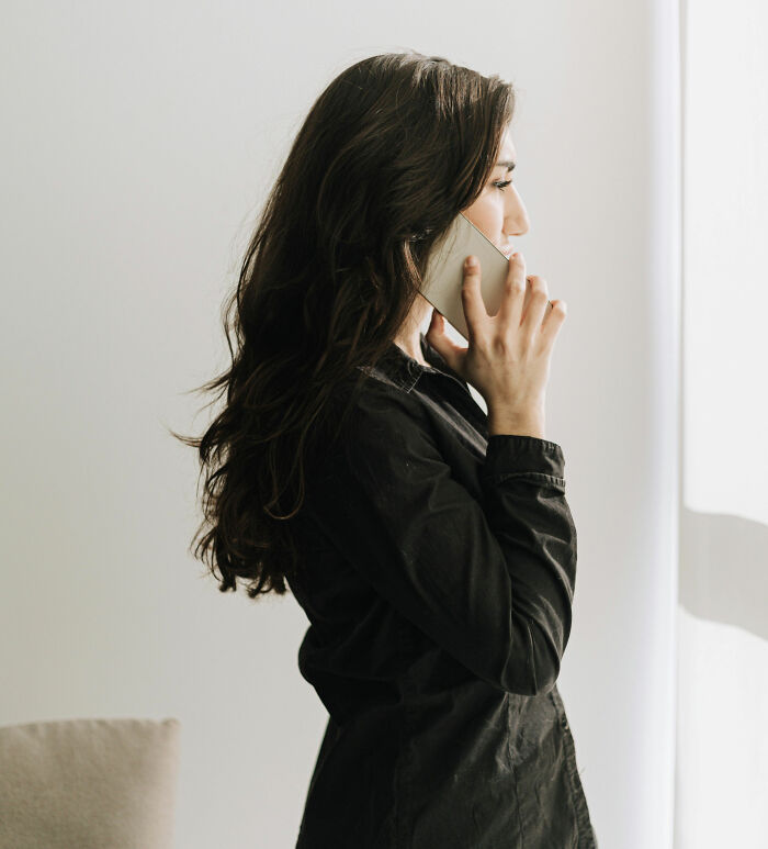Therapist with long dark hair talking on smartphone in a bright room, reflecting on surprising moments in therapy sessions.