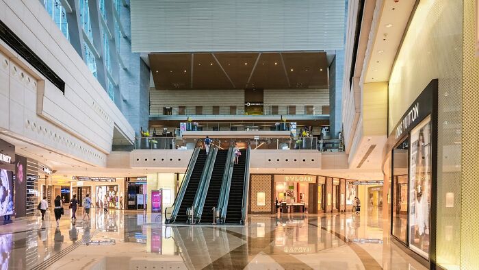 Spacious modern shopping mall interior with escalators and luxury brand stores, capturing memorable moments of presence.