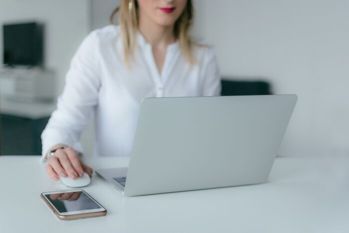 Woman in white shirt using laptop and mouse at desk with smartphone, illustrating companies that crashed after key person left.