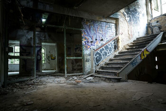 Abandoned explorers inside a creepy urban ruin with graffiti-covered walls and debris-strewn floors during their escapades.