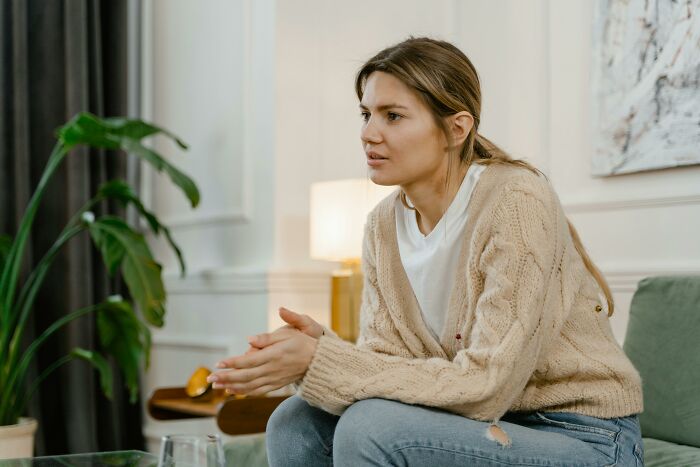 Young woman in beige sweater thoughtfully discussing dark truths of human behavior in a cozy living room setting