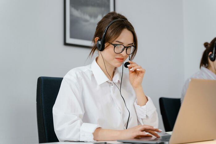 Young woman with headset working on laptop in an office, illustrating companies crashing when key person leaves.