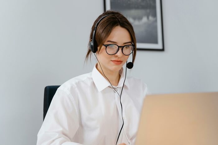 Young woman wearing headset and glasses working on laptop, showing a completely normal thing without any irrational ick feelings.
