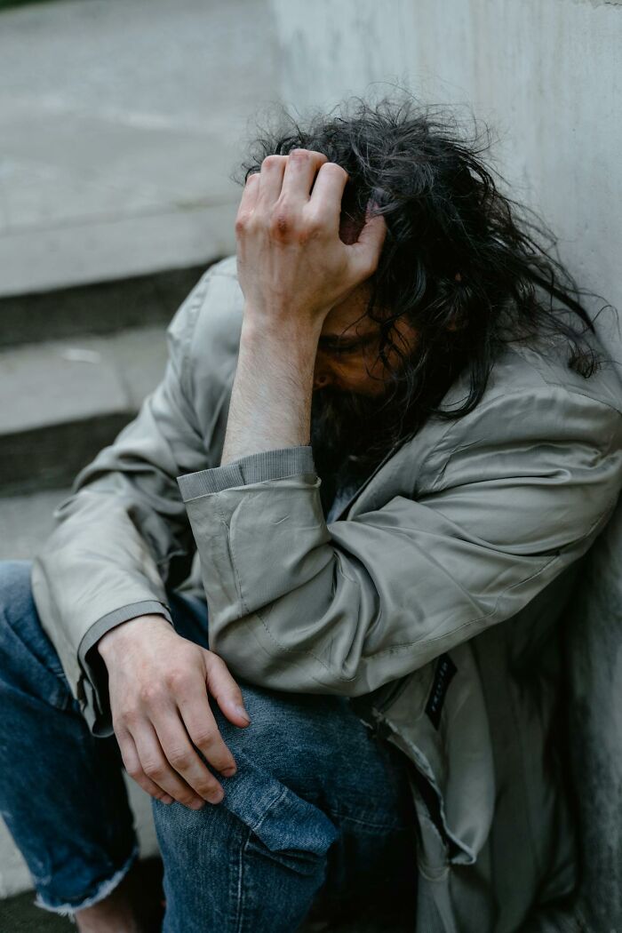 Man with disheveled hair and worn clothes sitting distressed against a wall, reflecting intense hospital experiences.