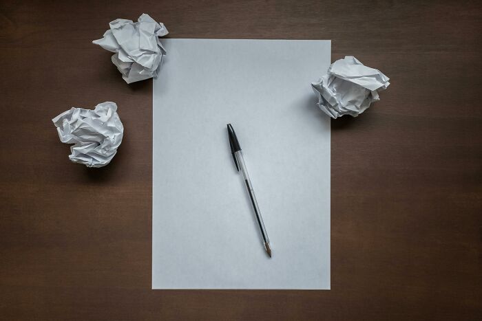 Blank sheet of paper with a pen on a wooden desk surrounded by crumpled paper balls representing afterlife theories.