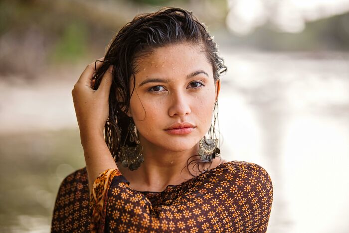 Young woman with wet hair and floral top making a tiny gesture that instantly charmed hearts outdoors by the water.