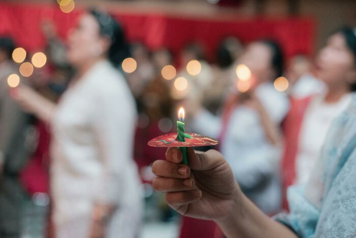 Person holding a lit candle during a social gathering, illustrating people still falling for fictional things.