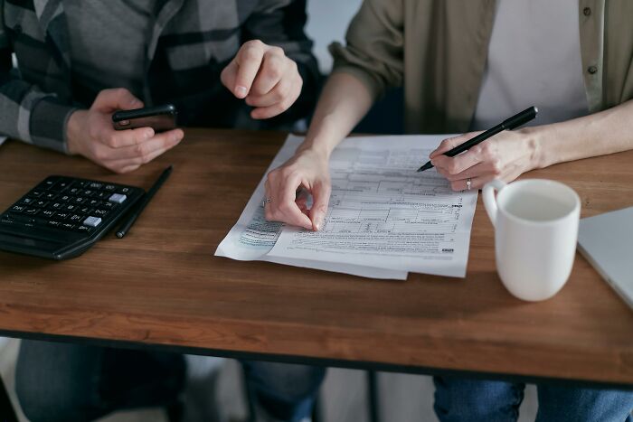 Two people reviewing documents at a wooden table with a calculator, pen, and white mug, sharing thoughts on the UK.