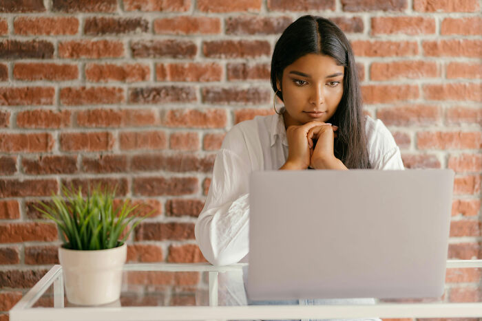 Woman reflecting deeply while using laptop, portraying feelings of cultural outsider and raising children alone. Woman reflecting deeply while using laptop, portraying feelings of cultural outsider and raising children alone.