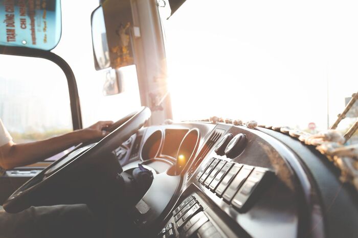 Truck driver gripping steering wheel inside a cab, bright sunlight streaming through the windshield during a drive.
