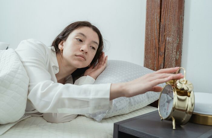 Person in white pajamas reaching to turn off alarm clock, illustrating a completely normal thing and irrational ick feeling.
