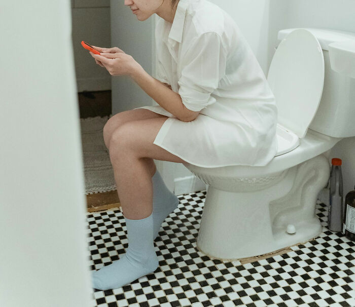 Person sitting on a toilet, focused on a smartphone, illustrating unique childhood joys lost with smartphones.