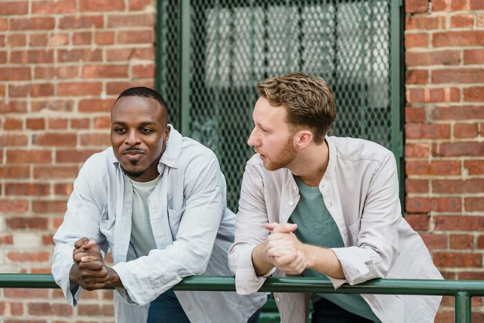 Two men leaning on a railing, sharing a moment of charm and connection through tiny gestures outdoors.
