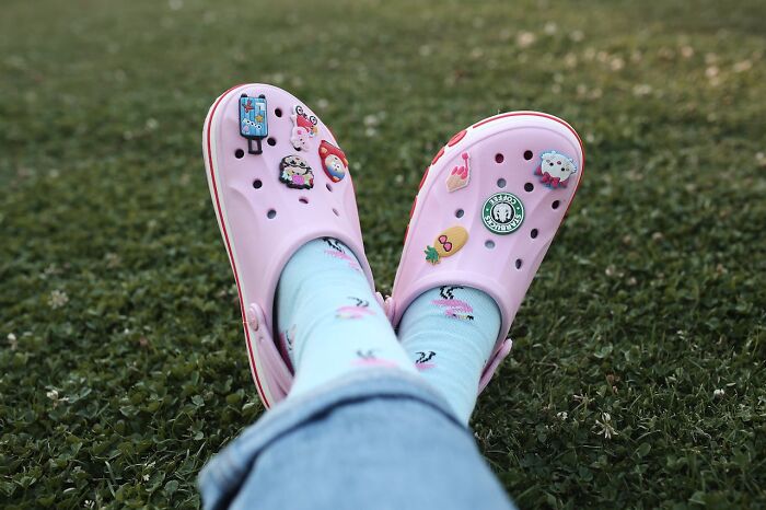 Person wearing pink Crocs with charms and blue socks with flamingos, relaxing on grass, representing women over 42 confident stance