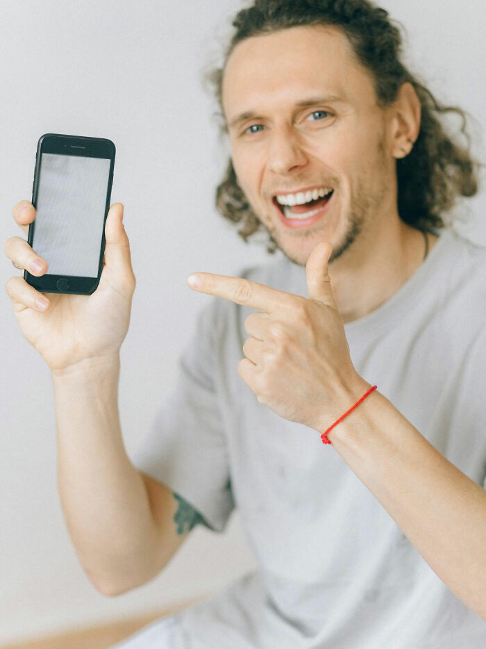 Smiling man with curly hair pointing at his smartphone, illustrating male coworkers sharing insane comments.