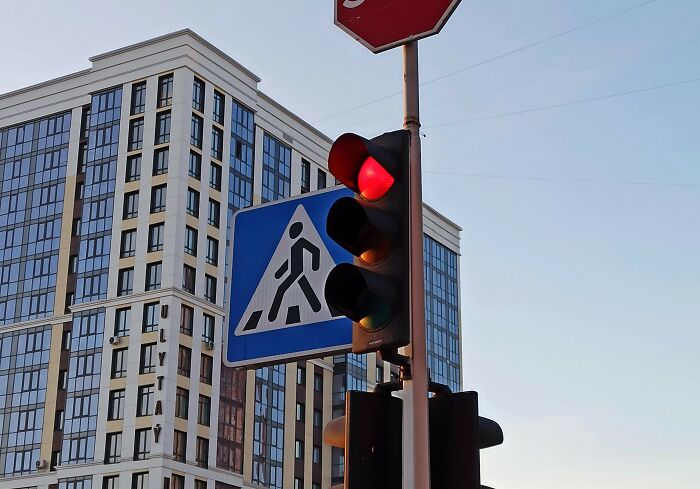 Traffic light showing red near a pedestrian crossing sign with a modern building in the background, illustrating legal caution.