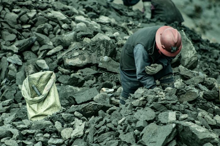 Worker wearing a hard hat sorting rocks in a rugged outdoor setting representing tough professions attracting awful people. - 29