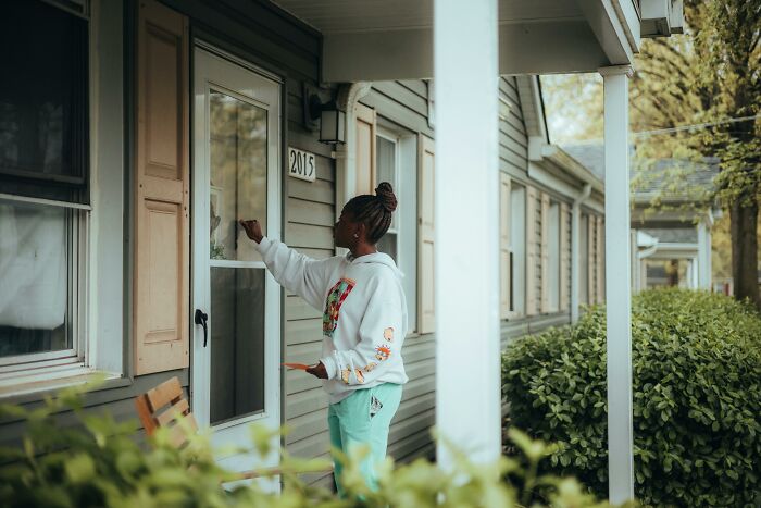 Person knocking on a front door of a suburban house numbered 2015, symbolizing a completely legal total psychopath scenario.