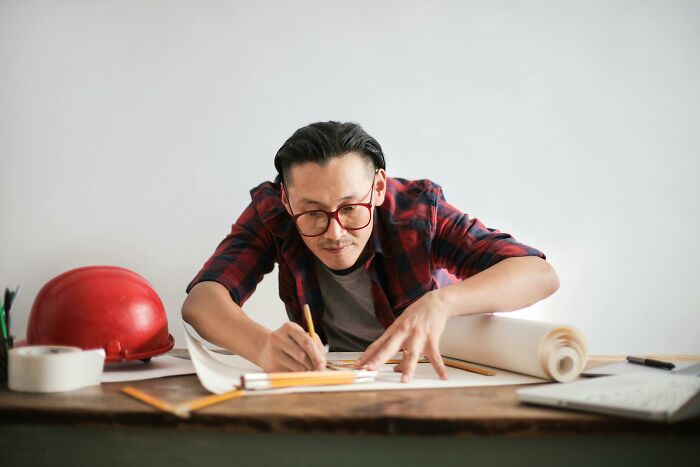 Man wearing red glasses focused on drawing plans at desk, illustrating the impact when the one person who knew stuff leaves.