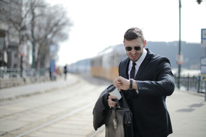 Man in a suit checking watch with coffee cup and briefcase, illustrating casual and harmless looking habits risks.