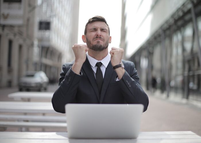 Man in suit sitting outdoors with laptop, showing excitement and clenching fists, representing private resort worker AMA.