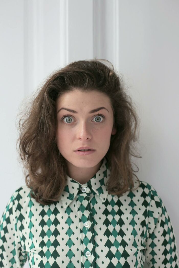 Young woman with expressive eyes in patterned shirt, reacting to insane things male coworkers told her at work.