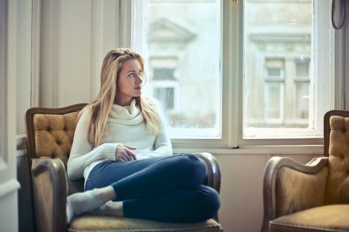 Woman sitting on vintage chair by window, relaxed and thoughtful, representing a private resort worker AMA insights.