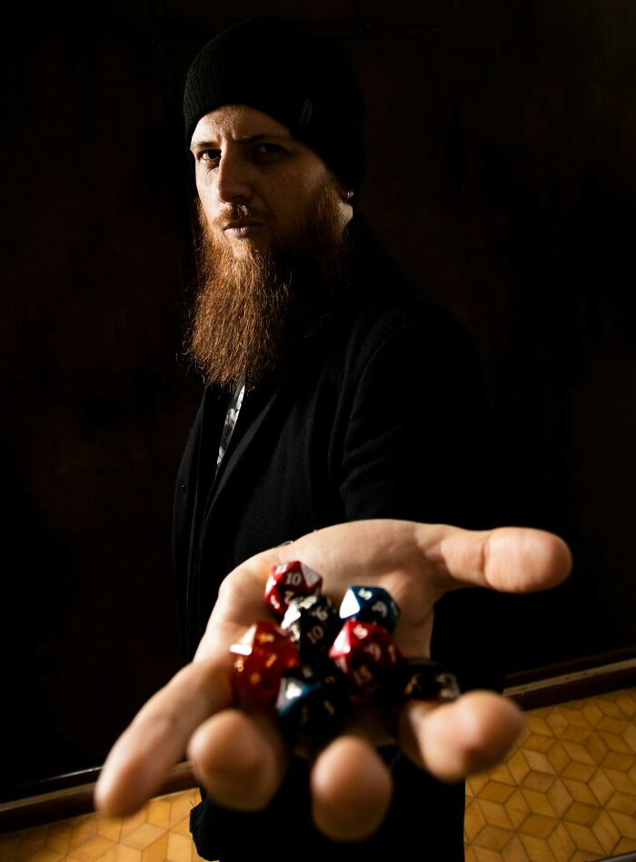 Man with a beard wearing a black hat holds colorful dice in his outstretched hand, capturing a shared moment experience.
