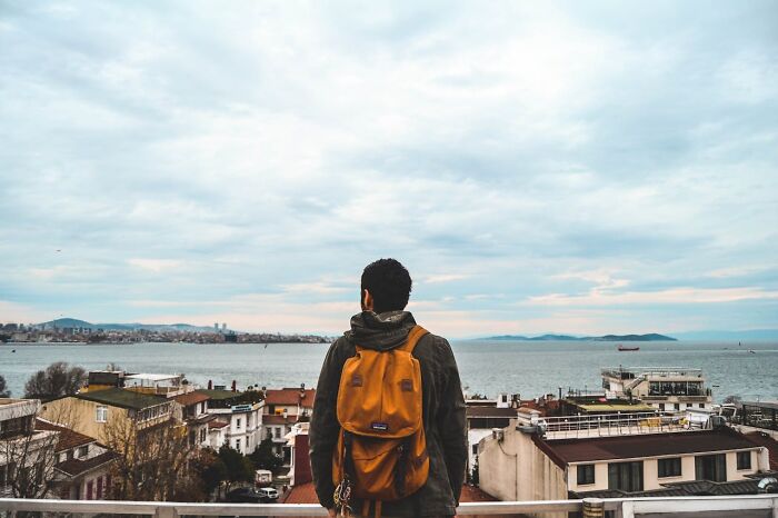Traveler with orange backpack overlooking city and sea, illustrating travel destinations tourists suggest avoiding.
