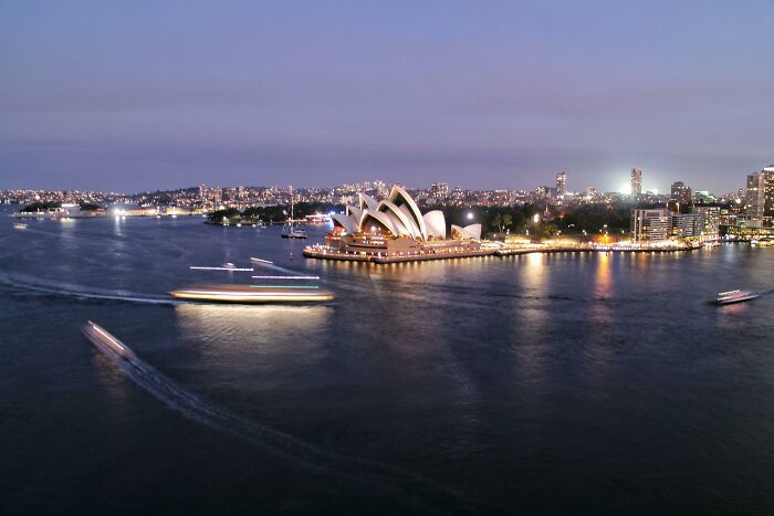 Sydney Opera House lit at dusk with ferries moving on harbor, illustrating normal sights that would shock most Americans.