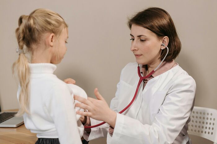 Female doctor using stethoscope to examine a young girl, illustrating coworker diabolical things report HR concept.