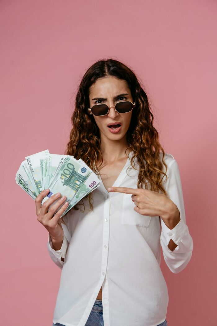 Woman in sunglasses holding euro bills, expressing surprise, representing private resort worker during an ask me anything session.
