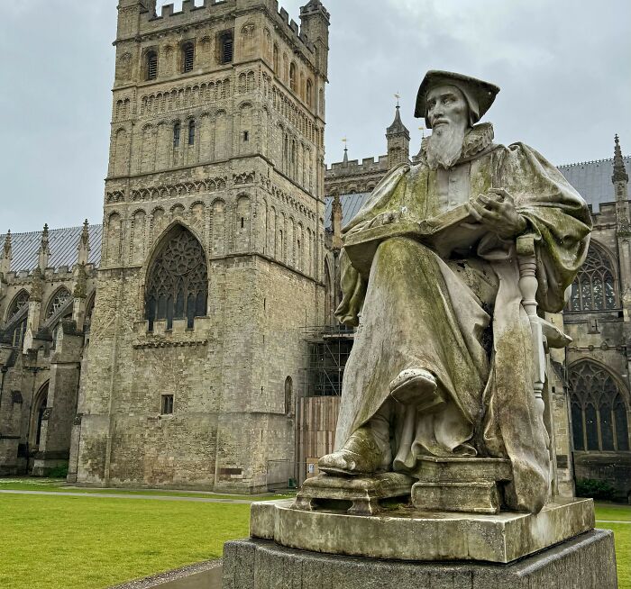 Stone statue of a historic figure outside a large Gothic-style cathedral in the UK, reflecting British culture and heritage.