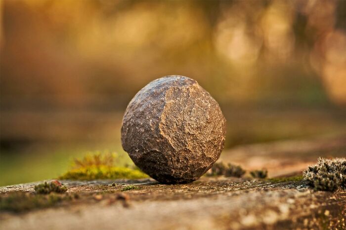Close-up of a weathered iron ball resting on mossy stone, capturing tiny gestures that instantly charm people's hearts.