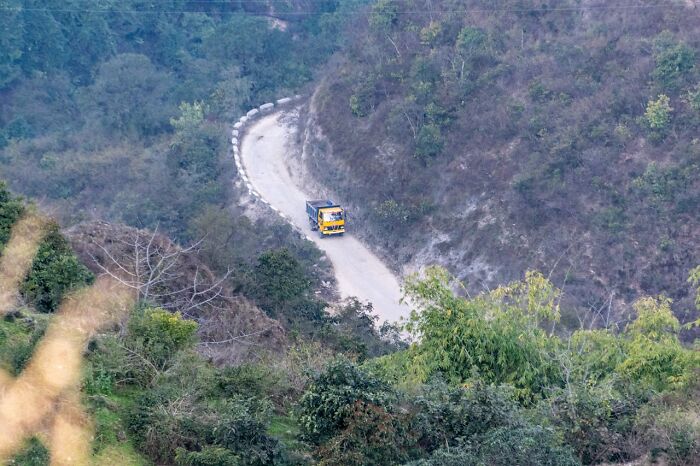 Yellow truck driving on a narrow winding mountain road surrounded by dense green trees and vegetation, creepy and scary moment.