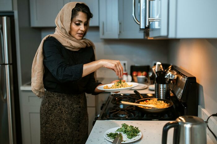 Woman wearing a headscarf cooking in kitchen, representing wife adopting husband’s culture while raising three kids alone. Woman wearing a headscarf cooking in kitchen, representing wife adopting husband’s culture while raising three kids alone.