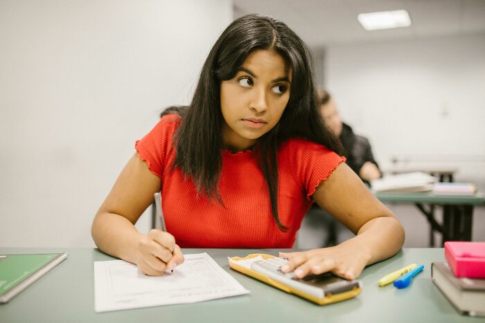 Teen girl in red shirt solving math problems using a calculator, focused on a high school math quiz.