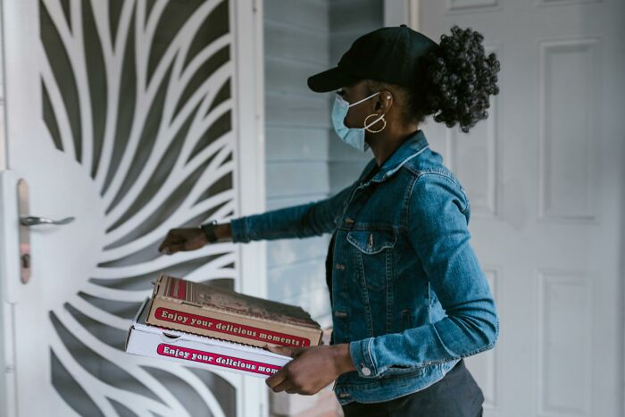 Woman wearing mask delivering pizzas at doorstep, illustrating uncommon hacks for women living alone.