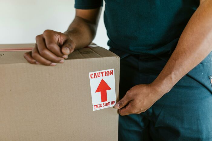 Person carefully placing a caution label on a cardboard box, showing tiny gestures that instantly charm hearts.