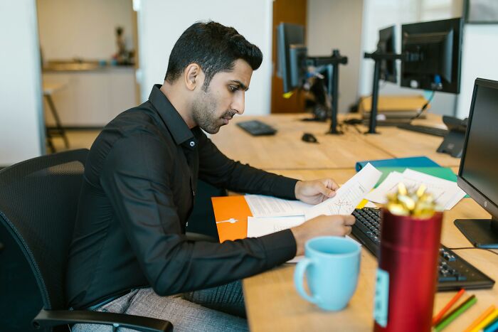 Man focused on paperwork at office desk with computer monitors, illustrating privilege and real world understanding.