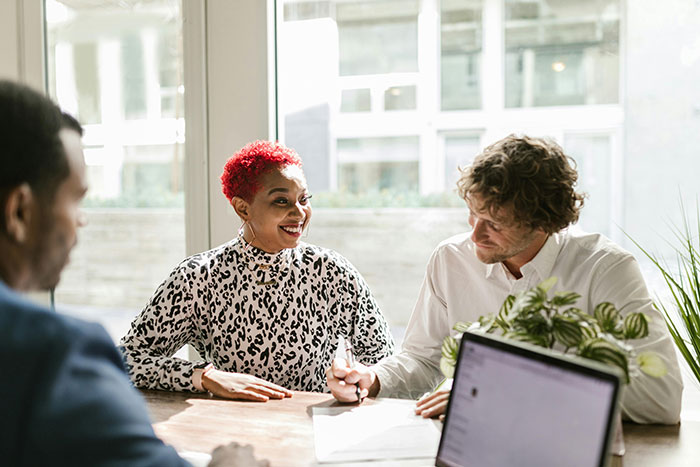 A man and woman having a discussion in an office, illustrating tensions about refusing a wife&rsquo;s work husband on family vacation.