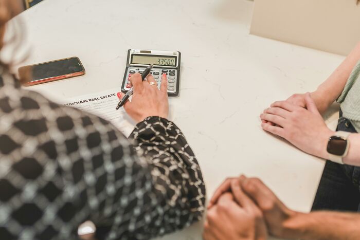 Two people calculating hidden costs of buying a home using a calculator and purchase agreement on a white table.