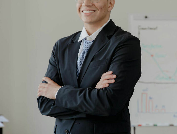 Young male coworker in business suit smiling with arms crossed in office, relating to insane things male coworkers said.