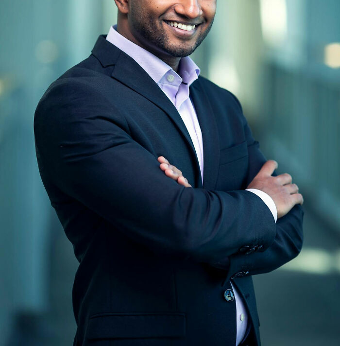 Smiling male coworker in business attire standing with arms crossed in an office, reflecting workplace interactions.