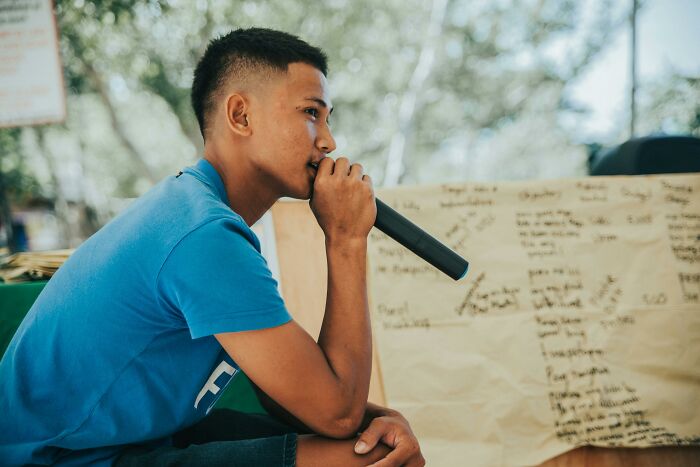 Young man holding a microphone and thinking, illustrating the challenge to prove you are smarter by guessing languages in a quiz.