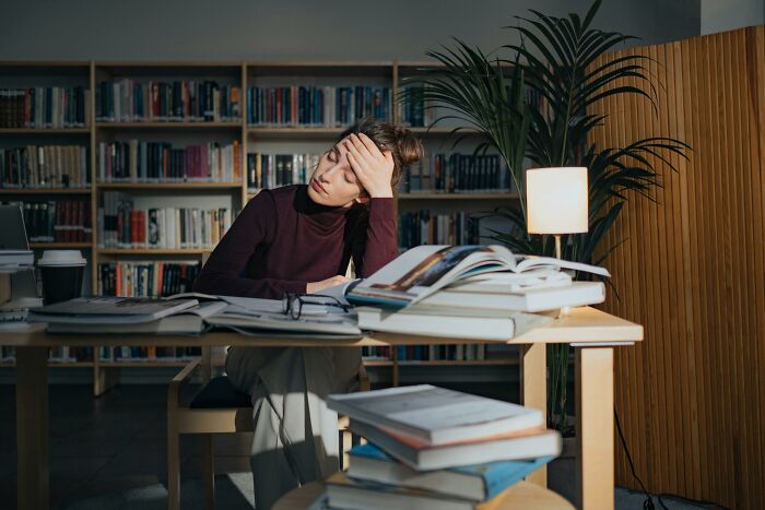 Woman sitting at a desk surrounded by books, showing signs of fatigue, illustrating casual habits potentially damaging long term.