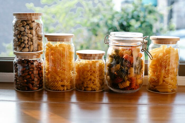 Various dry foods like nuts and pasta stored in glass jars on a sunlit windowsill, illustrating poor people habits.